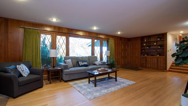 living room featuring light hardwood / wood-style flooring, built in shelves, and wood walls