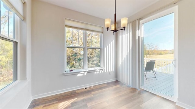 unfurnished dining area with an inviting chandelier, wood-type flooring, and a wealth of natural light