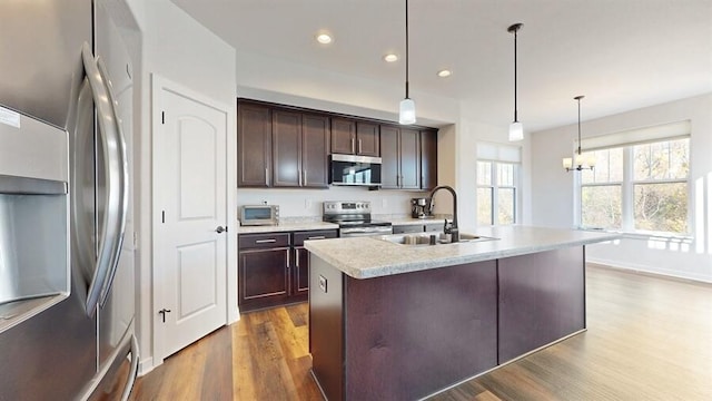 kitchen featuring appliances with stainless steel finishes, sink, dark hardwood / wood-style flooring, hanging light fixtures, and a center island with sink