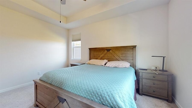 bedroom with a raised ceiling, light colored carpet, and ceiling fan