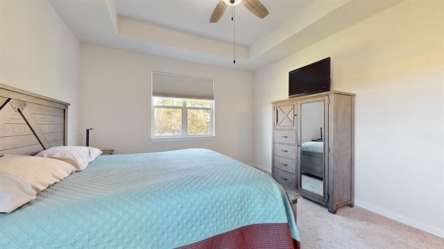 bedroom with light colored carpet, a tray ceiling, and ceiling fan