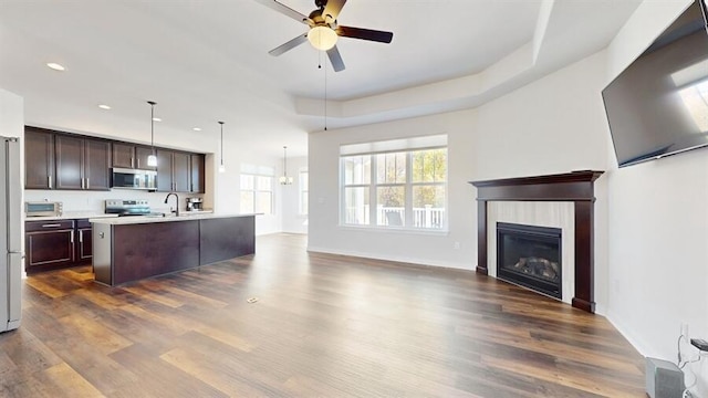 kitchen with dark hardwood / wood-style floors, appliances with stainless steel finishes, decorative light fixtures, and a center island with sink