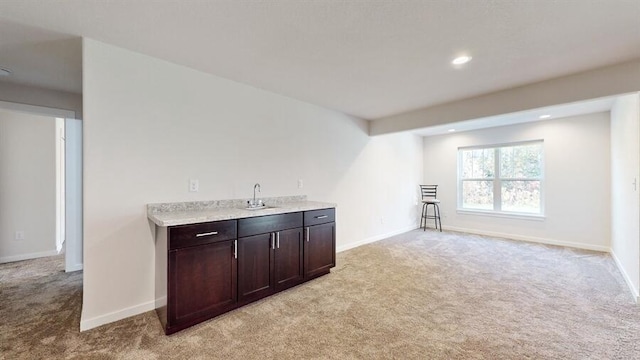 bar with dark brown cabinetry, sink, and light colored carpet