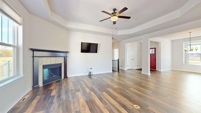 unfurnished living room with ceiling fan with notable chandelier, a tile fireplace, a raised ceiling, and dark hardwood / wood-style flooring