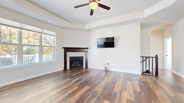 unfurnished living room featuring ceiling fan, dark wood-type flooring, a fireplace, and a raised ceiling