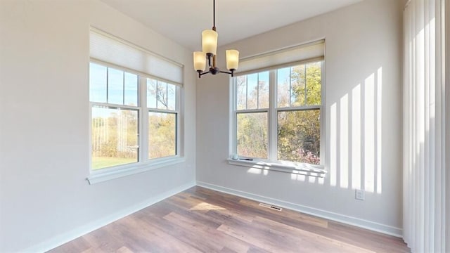 unfurnished dining area with hardwood / wood-style floors, a notable chandelier, and a healthy amount of sunlight