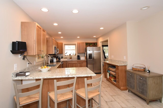 kitchen with stainless steel appliances, light stone countertops, kitchen peninsula, and a kitchen bar