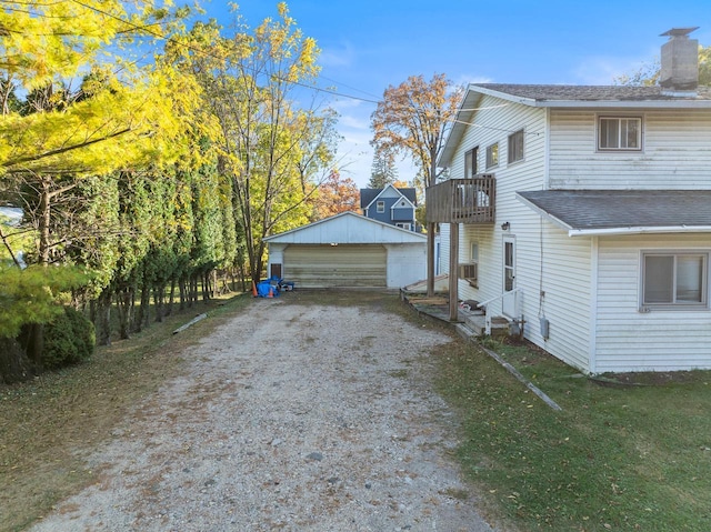 view of side of property with roof with shingles, a detached garage, a chimney, a balcony, and an outdoor structure