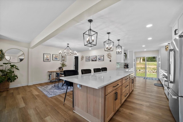 kitchen with a large island, white cabinetry, a kitchen bar, pendant lighting, and light hardwood / wood-style floors