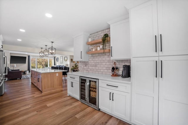 kitchen with light wood-type flooring, a kitchen island, hanging light fixtures, white cabinetry, and beverage cooler