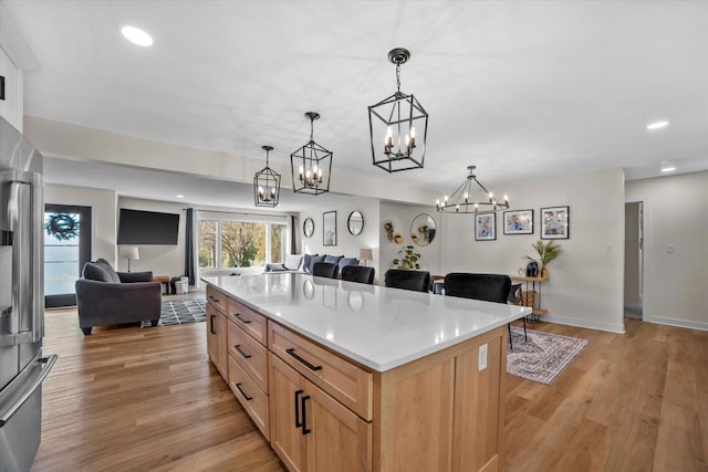 kitchen featuring a center island, decorative light fixtures, stainless steel refrigerator, light hardwood / wood-style flooring, and light brown cabinets