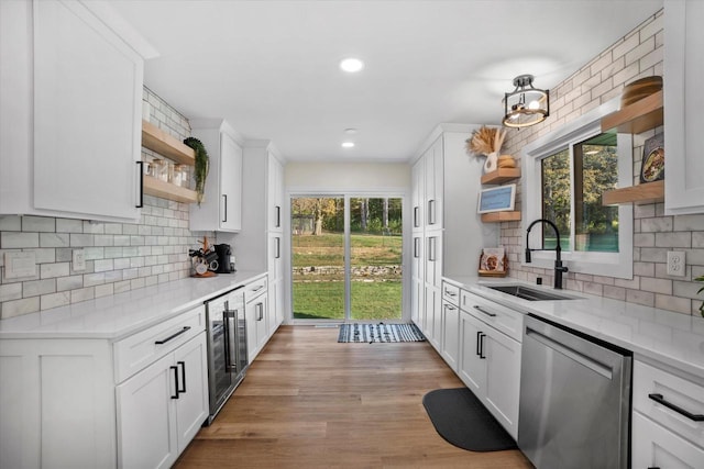 kitchen featuring stainless steel dishwasher, sink, white cabinetry, and beverage cooler