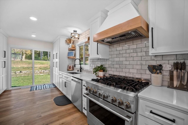 kitchen featuring custom range hood, stainless steel appliances, white cabinetry, and plenty of natural light