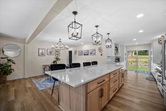 kitchen featuring tasteful backsplash, hanging light fixtures, a kitchen breakfast bar, light brown cabinetry, and light hardwood / wood-style floors