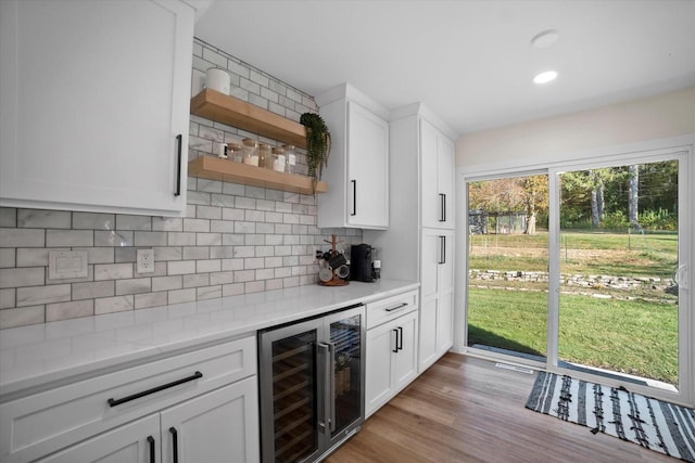 kitchen featuring white cabinets, tasteful backsplash, beverage cooler, light hardwood / wood-style flooring, and light stone counters