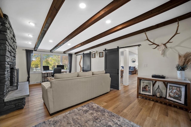 living room featuring light hardwood / wood-style floors, beam ceiling, and a barn door