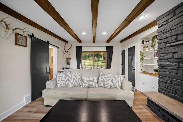 living room with beamed ceiling, a barn door, and light wood-type flooring