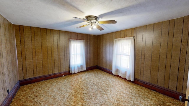 carpeted spare room featuring wooden walls, plenty of natural light, and ceiling fan