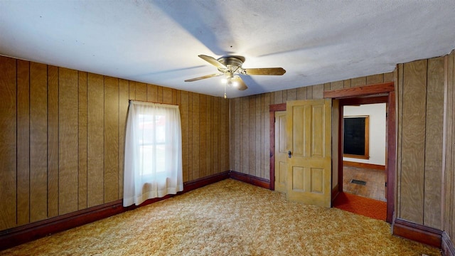 carpeted empty room with wood walls, a textured ceiling, and ceiling fan