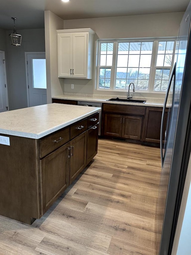 kitchen with stainless steel refrigerator, sink, light hardwood / wood-style flooring, pendant lighting, and white cabinets