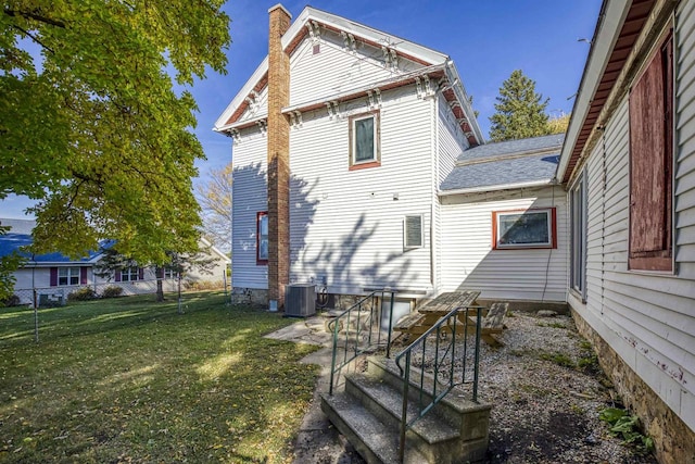 rear view of house with central AC and a lawn