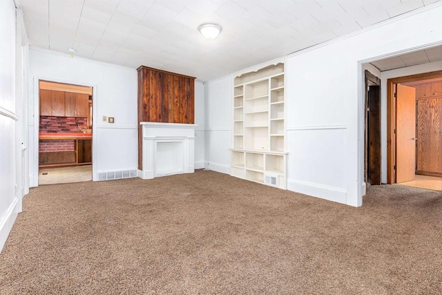 unfurnished living room featuring ornamental molding, carpet floors, and built in shelves