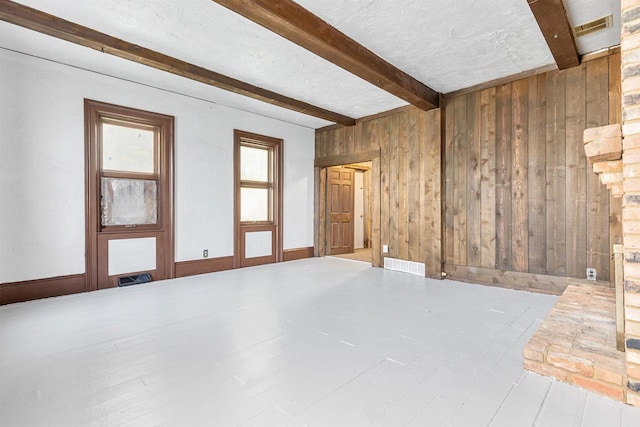 unfurnished room with beam ceiling, wooden walls, wood-type flooring, and a textured ceiling