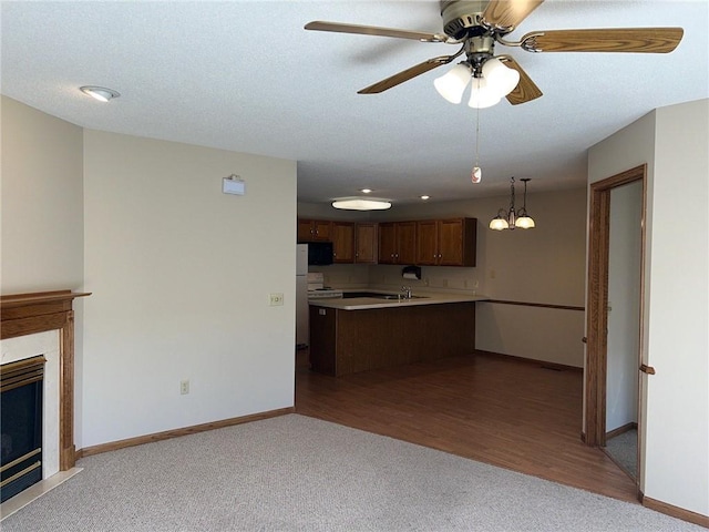 kitchen featuring kitchen peninsula, hanging light fixtures, light wood-type flooring, ceiling fan with notable chandelier, and sink