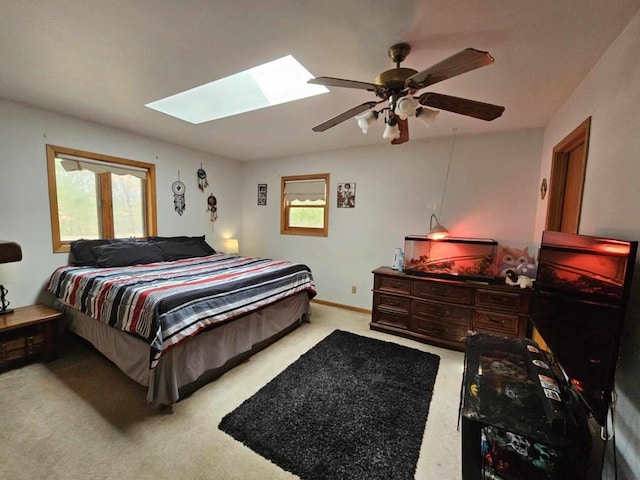 bedroom with a skylight, a ceiling fan, baseboards, and light carpet