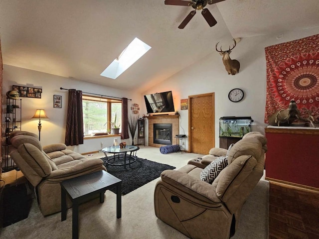 carpeted living area featuring a tiled fireplace, vaulted ceiling with skylight, baseboards, and ceiling fan