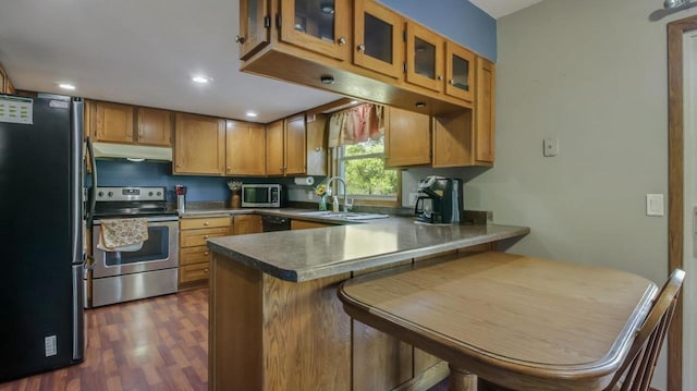 kitchen featuring appliances with stainless steel finishes, sink, a kitchen bar, kitchen peninsula, and dark hardwood / wood-style floors