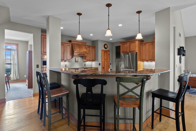 kitchen with appliances with stainless steel finishes, dark stone counters, a kitchen bar, and light hardwood / wood-style floors