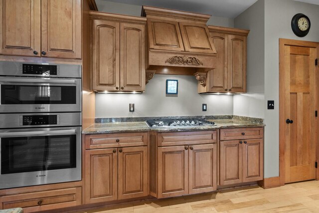 kitchen with dark stone countertops, stainless steel appliances, light wood-type flooring, and custom exhaust hood