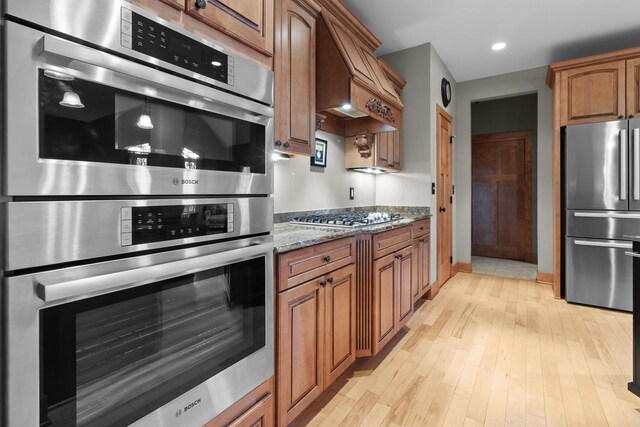 kitchen with premium range hood, light hardwood / wood-style flooring, light stone counters, and stainless steel appliances