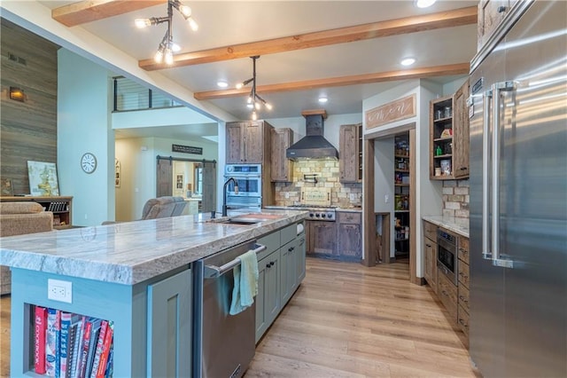 kitchen with beamed ceiling, wall chimney exhaust hood, stainless steel appliances, and an island with sink