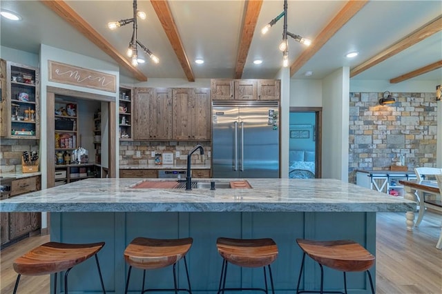 kitchen with stainless steel built in refrigerator, beam ceiling, a large island, light stone countertops, and light hardwood / wood-style floors