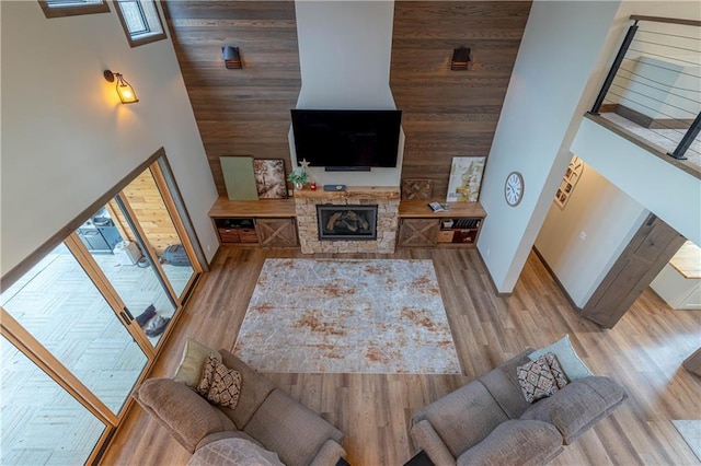 living room featuring a stone fireplace, light hardwood / wood-style flooring, wooden walls, and a high ceiling