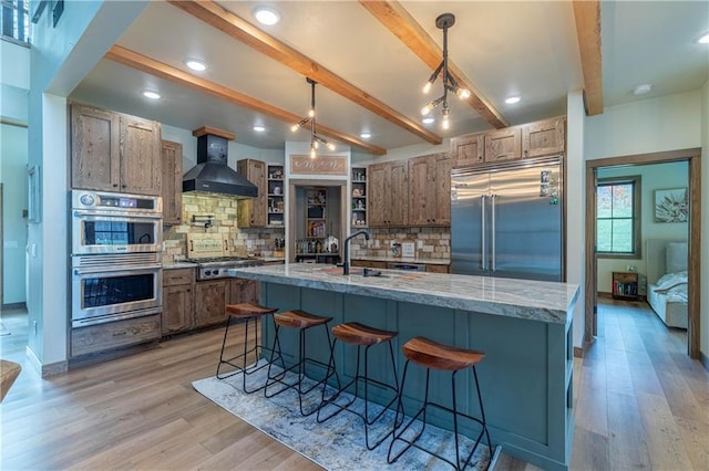 kitchen with wall chimney range hood, beam ceiling, backsplash, appliances with stainless steel finishes, and decorative light fixtures