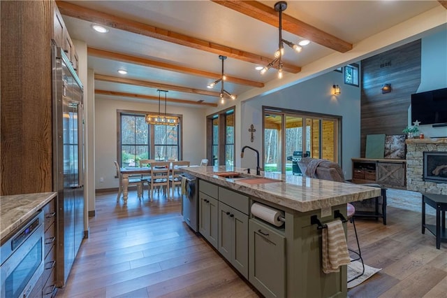 kitchen featuring sink, light hardwood / wood-style floors, pendant lighting, built in appliances, and a kitchen island with sink