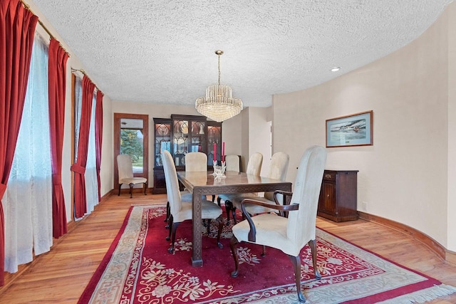 dining space with a textured ceiling, a chandelier, and light wood-type flooring