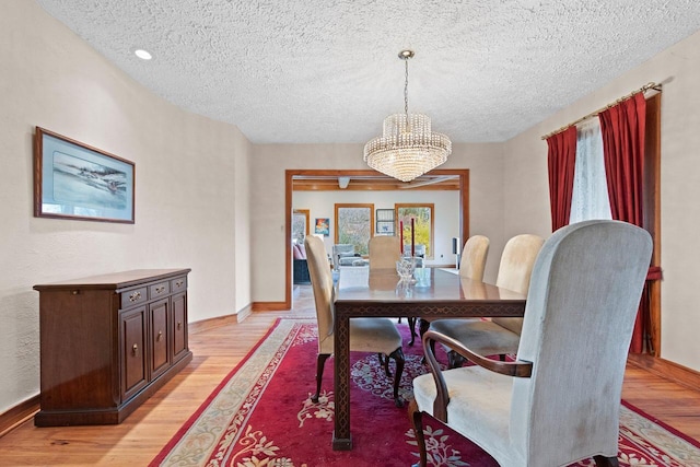 dining space with light hardwood / wood-style flooring, a notable chandelier, and a textured ceiling