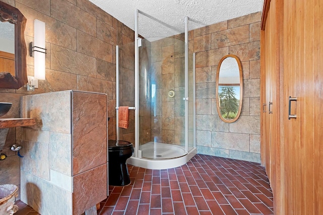 bathroom with a shower with door, a textured ceiling, toilet, and tile walls