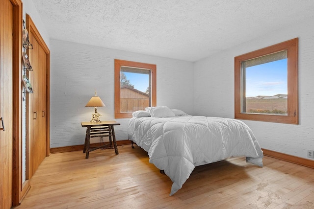 bedroom with light hardwood / wood-style flooring, a textured ceiling, and multiple windows