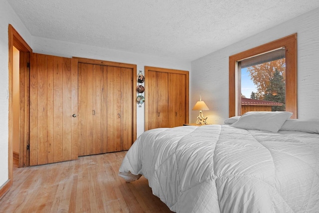 bedroom featuring light hardwood / wood-style floors, multiple closets, and a textured ceiling