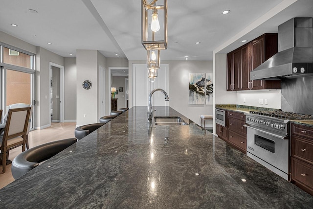 kitchen featuring appliances with stainless steel finishes, dark stone counters, pendant lighting, wall chimney exhaust hood, and sink