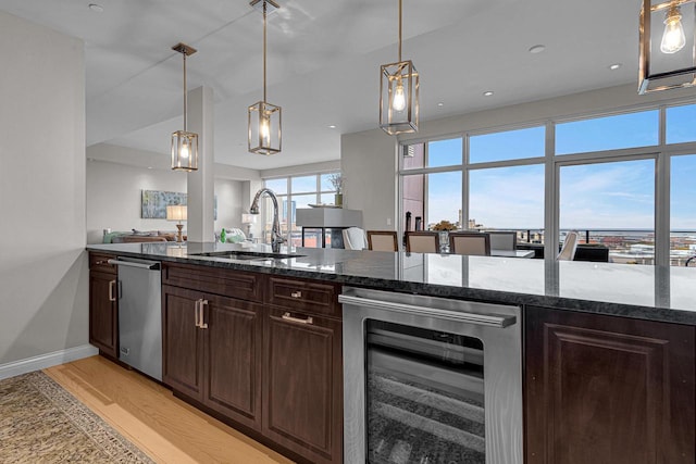 kitchen featuring light hardwood / wood-style flooring, dark stone counters, wine cooler, sink, and dark brown cabinetry