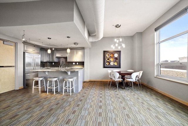 kitchen with decorative backsplash, a breakfast bar area, stainless steel refrigerator, gray cabinets, and decorative light fixtures