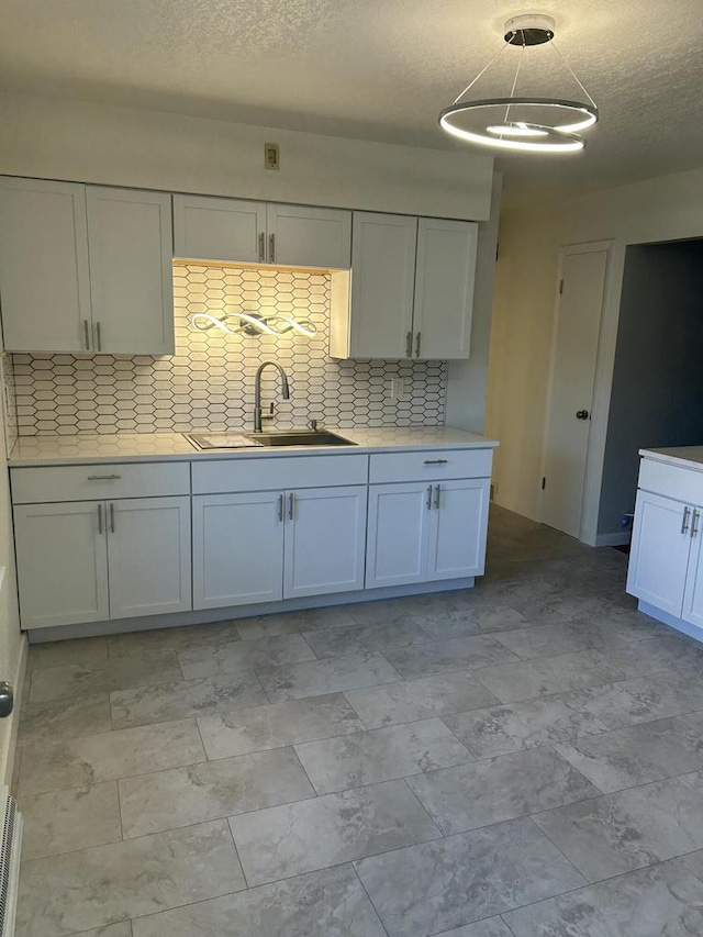 kitchen featuring sink, white cabinets, a textured ceiling, and backsplash