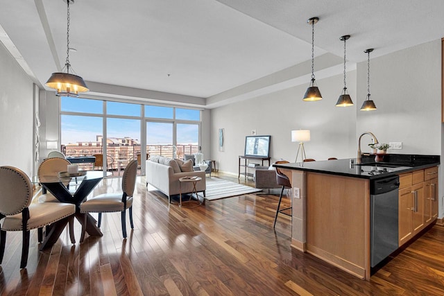 kitchen with dishwasher, a kitchen island with sink, dark wood-type flooring, sink, and decorative light fixtures