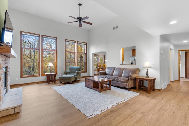 living room featuring ceiling fan, vaulted ceiling, light wood-type flooring, and a fireplace